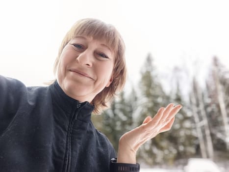 Middle-aged female blogger poses for a selfie amid snowy scenery, embracing her journey of exploration and travel.