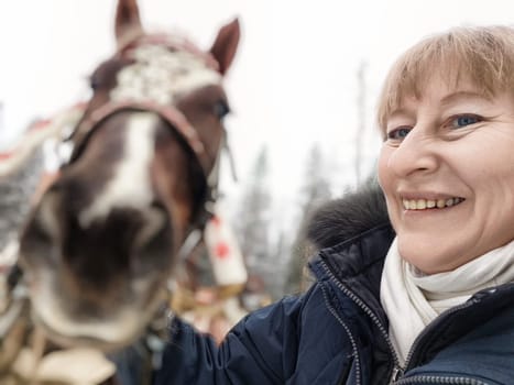 A woman takes a joyful selfie with a horse, capturing her excitement while exploring the great outdoors in winter.