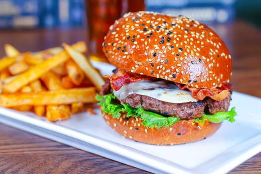A Cheese, Bacon hamburger with french fries on a white plate.