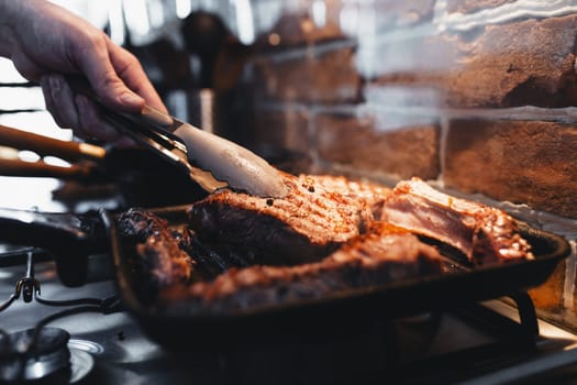 Hand turns steak with tongs during preparation on the grill pan with seasonings. High quality photo