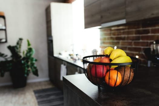 Tropical fruits: broken coconut, apple, tangerine, orange, banana in fruit bowl on bar counter in stylish loft kitchen. Blurred background. High quality photo