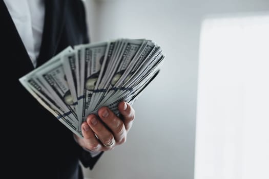 One hundred dollar bills money fun, in hand of man in suit and white shirt. Blurred background. High quality photo