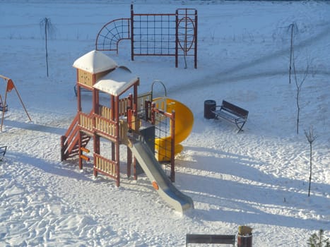 playground in the morning in winter in the snow lit by the sun is waiting for children and parents
