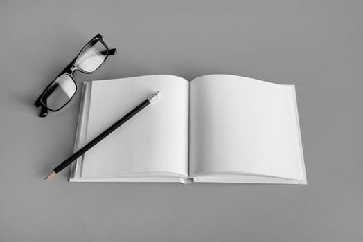Mockup of opened blank brochure, pencil and glasses on gray paper background. Responsive design template.