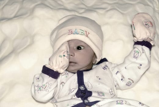 Closeup portrait image of cute beautiful adorable baby boy Asian Indian ethnicity in winter clothing lying of bed on white blanket. Sweet toddler posing looking in surprised curious mood. Front View.