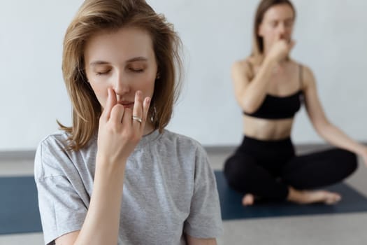 Two athletic attractive girls sit in lotus position on yoga mat indoors .Yoga, fitness and healthy lifestyle.