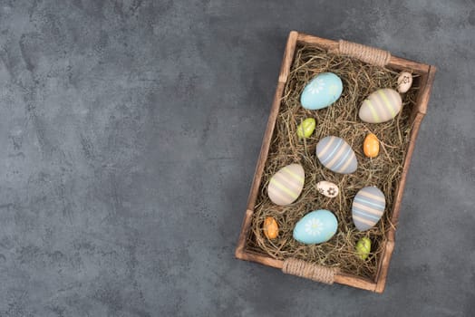 Colored easter eggs in a basket with hay, empty copy space for text