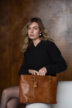 A girl in a warm sweater, a black short skirt, nylon tights, black loafers and gray socks is posing with a brown bag