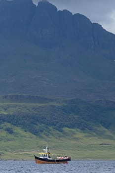 Rock formation named the old man of storr, on the isle of skye, looms imposingly over a small wooden fishing boat. Very dramatic scottish coastline.
