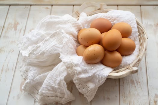 Chicken eggs in basket on white shabby wooden table