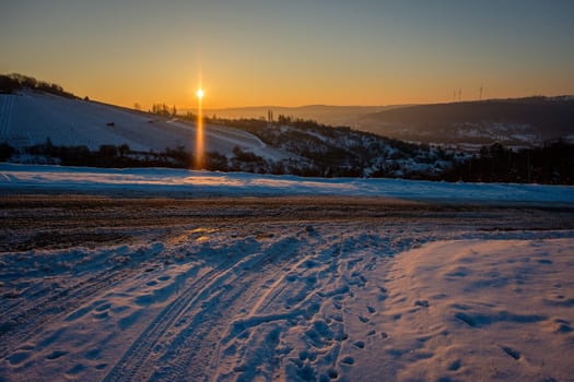 Road with snow in winter vineyard landscape and back lit
