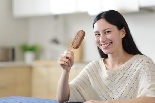 Asian woman holding ice cream looking at camera in a kitchen at home
