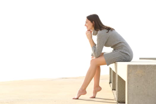 Profile of a beautiful woman with long waxed legs sitting in a bench with white background in winter