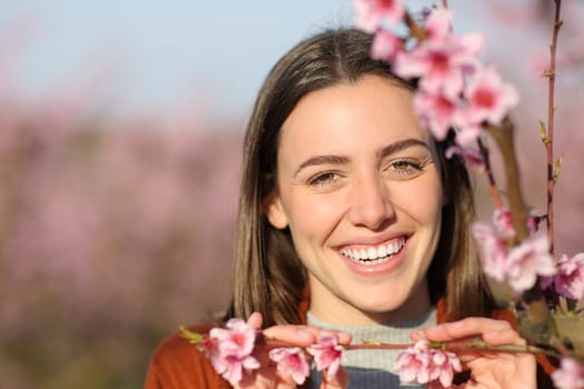 Front view portrait of a happy woman smiling between flowers in a field looking at you