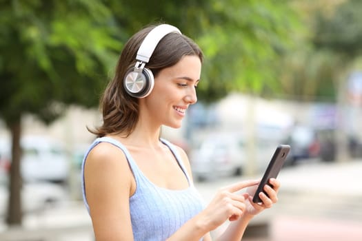 Happy woman using phone and headphone walking in a park