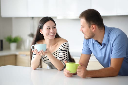Interracial couple talking and drinking in the kitchen at home