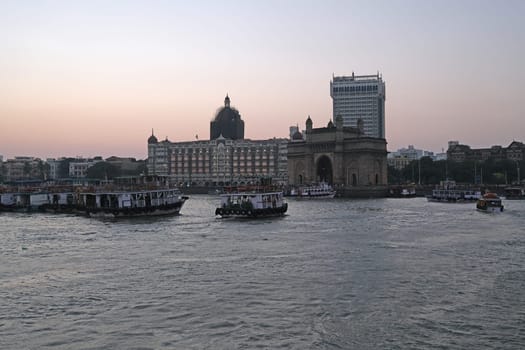 Taj Mahal hotel, Gateway of India and tourist boats in water of Arabian Sea on sunset in Mumbai, India