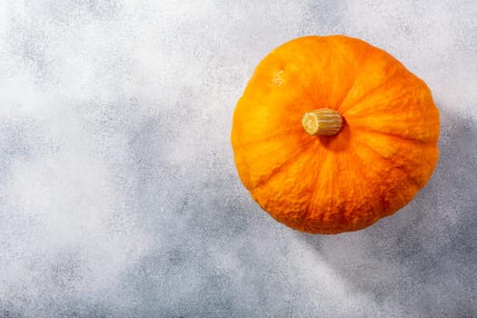 Orange pumpkin (Cucurbita pepo fruit) on grey textured backdrop w/ copy space, top view
