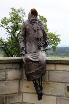 Monk Maurus with a violin sitting on the wall around the church in parish church of St. James in Hohenberg, Germany