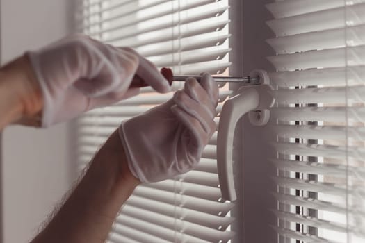 Close-up of hands in gloves with screwdriver, installing a new handle.