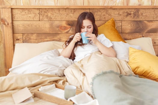 Young relaxing woman in bed in the morning with a mug of tea.