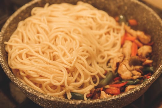 Fried noodles with vegetables and turkey meat in a black iron wok pan on