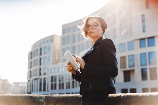 Portrait of a young woman with glasses, a knitted hat and a black leather jacket with an electronic tablet. Street photos