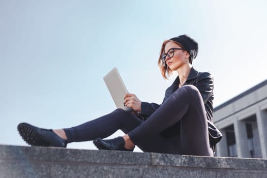 A young hipster woman enjoys a tablet on the street in the city.