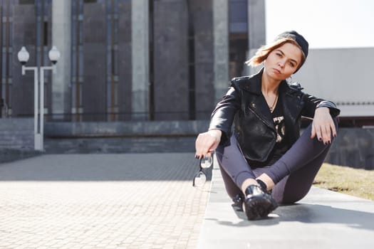 Portrait of fashionable blonde girl with eye glasses wearing a rock black style outdoors in the city