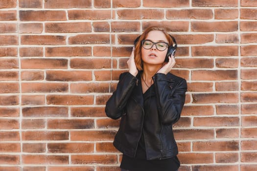 Portrait of a blondhair cheerful young woman enjoying music in headphones over brick grunge wall background