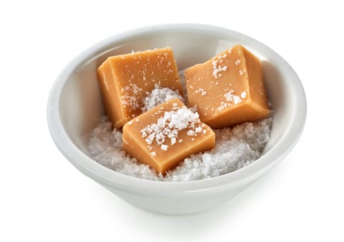 Pieces of creamy caramel fudge in a bowl of coarse salt over a white background in a high angle view