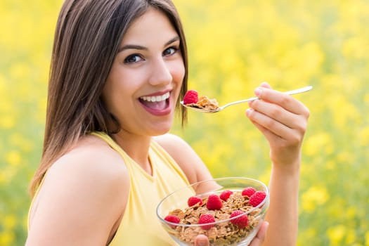 Close up face shot of attractive young woman eating healthy crispy whole grain cereal breakfast outdoors.