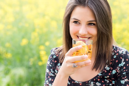 Close up portrait of attractive girl drinking ice tea outdoors against yellow flower background.
