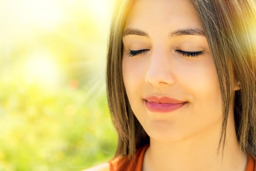 Close up portrait of attractive relaxed young woman meditating outdoors.Girl with eyes closed against bright colorful outdoor background.