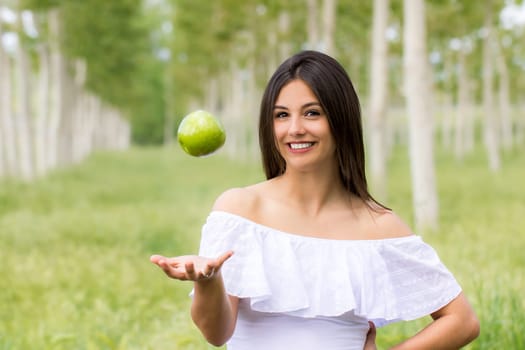 Close up portrait of cute young woman throwing green apple in air outdoors.