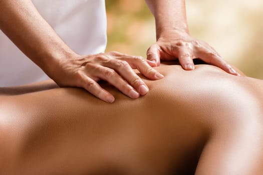 Close up detail of hands doing physiotherapy on female spine against colorful background.