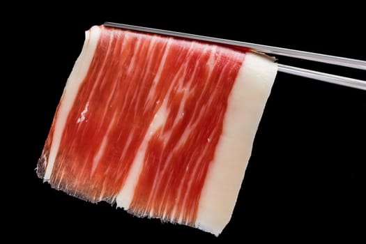 Extreme macro close up of cut piece of cured Spanish bellota pork ham on tweezer.