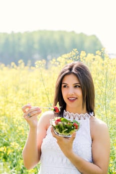 Close up portrait of cute young woman eating green salad in flower field.