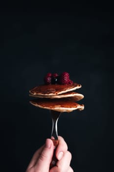 Hand holds a fork with juicy pancakes with berries and honey. High quality photo