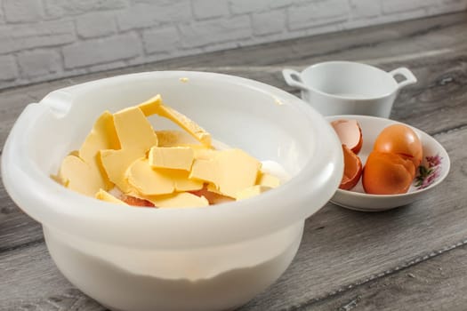 White plastic bowl with butter, egg yolk, flour and salt, ready to be mixed - preparation for baking a cake.