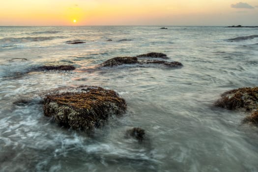 Long exposure shot of rocks covered with algae and sea weed not covered by sea during low tide, in sunset light. Koh Lanta, Thailand