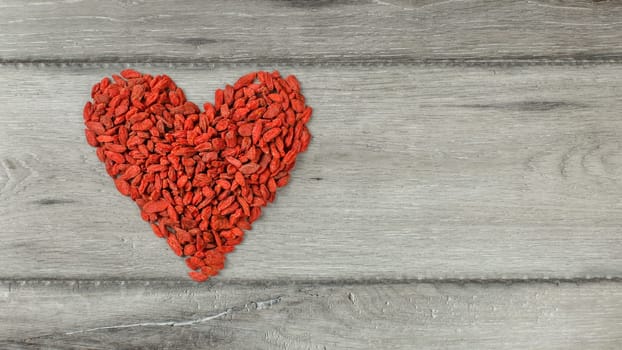 Top view on heart shape symbol made of goji (wolfberry) berries on gray wood desk