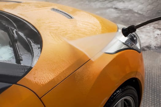 Yellow car front washed by water jet spray in carwash.