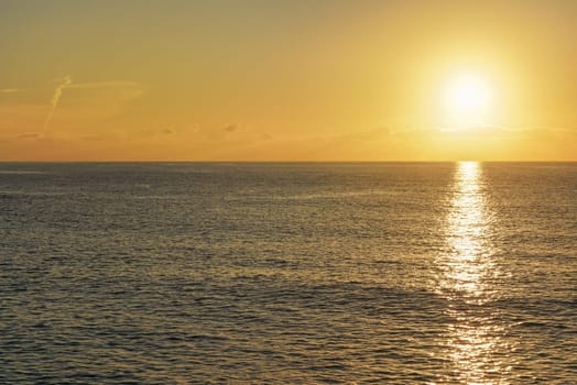 Sun rising above calm sea, clouds coloured to orange.