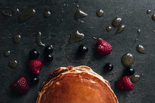 Juicy pancakes with berries, honey, spoon on a black and gray concrete table. High quality photo