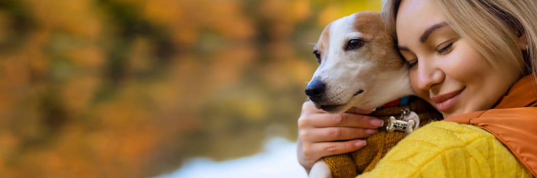 Portrait of a smiling young woman kissing a dog in a field. Dog lover stylish girl hugging her dog while walking. Animal friendship concept.