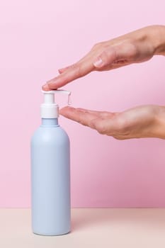 Female hands using alcohol gel sanitizer bottle dispenser, against coronavirus disease (Covid-19) . Antiseptic, Hygiene and Health concept. Minimalist style on pink background