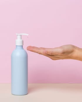 Female hand using alcohol gel sanitizer bottle dispenser, against coronavirus disease (Covid-19) . Antiseptic, Hygiene and Health concept. Minimalist style on pink background