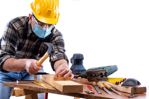 Carpenter worker at work isolated on white background, wears helmet, goggles, leather gloves and surgical mask to prevent coronavirus infection. Preventing Pandemic Covid-19 at the workplace.