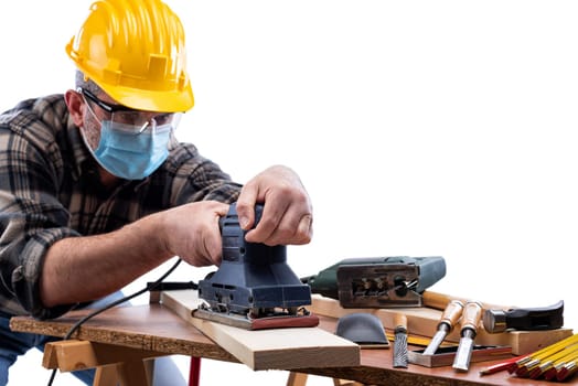 Carpenter worker at work isolated on white background, wears helmet, goggles, leather gloves and surgical mask to prevent coronavirus infection. Preventing Pandemic Covid-19 at the workplace.
